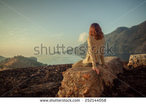 stock-photo-a-young-woman-is-sitting-on-an-unusual-rock-on-a-mountain-overlooking-a-bay-at-sunrise-in-a-252144058